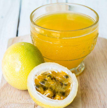 um copo de suco de maracujá e uma fruta inteira e outra pela metade ao lado do copo