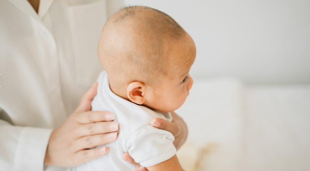 uma mão de uma médica sobre as costas do bebê sentado