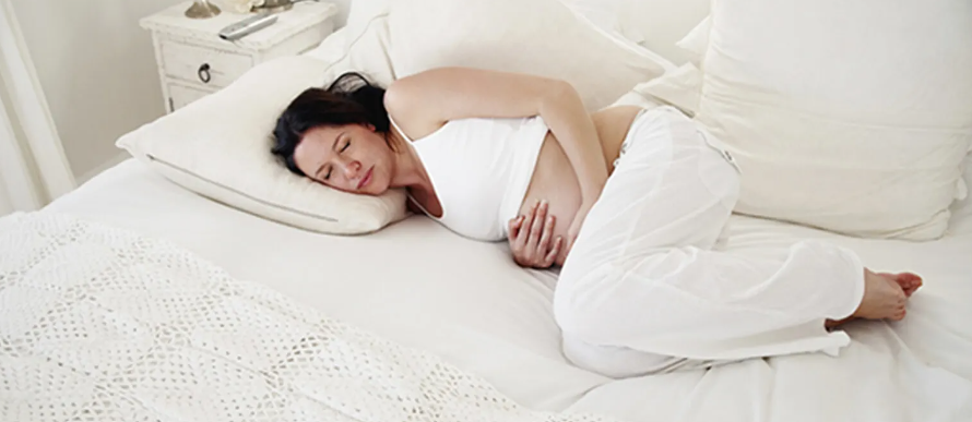 mulher grávida deitada na cama com as mãos na barriga com expressão de dor