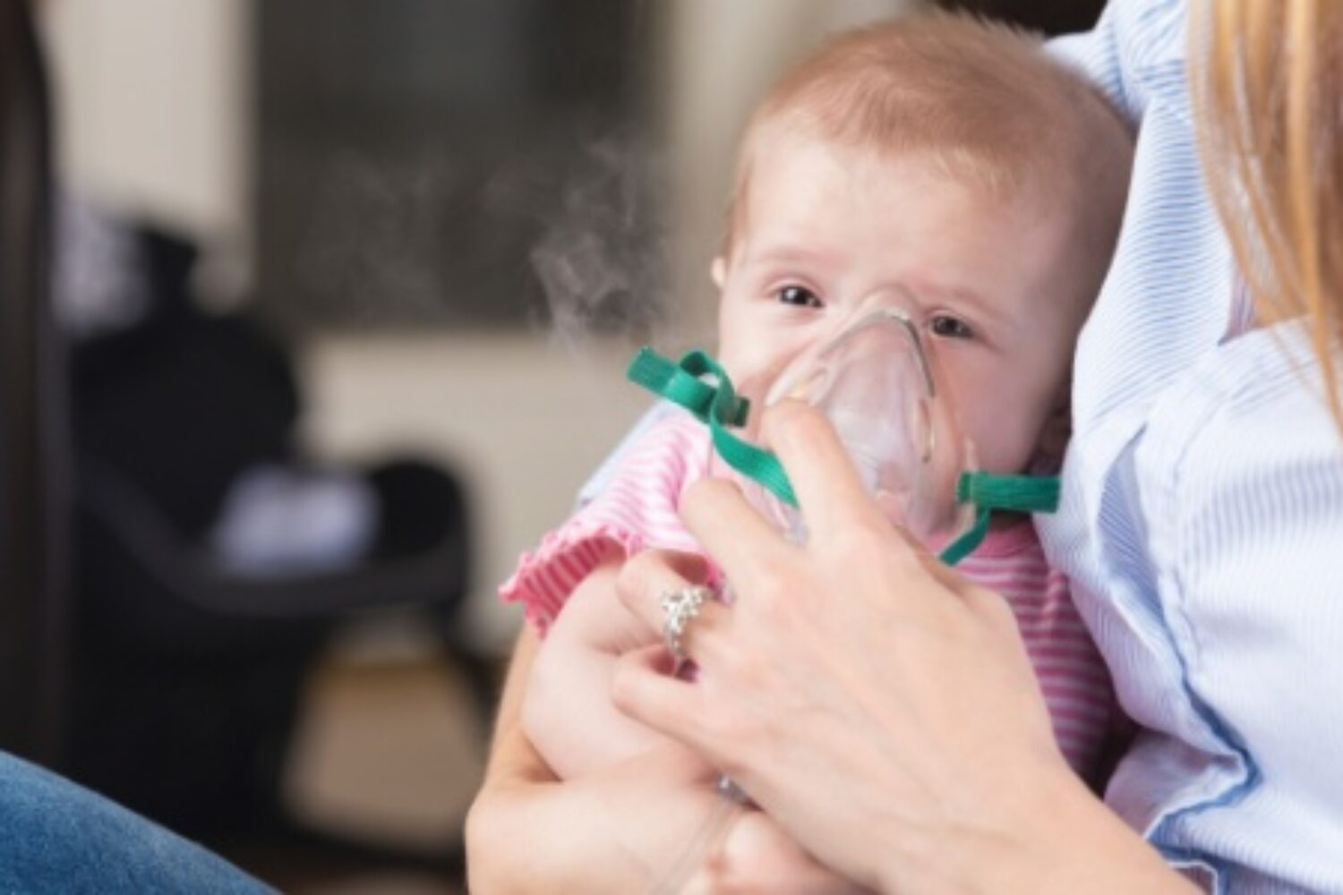 Bebê no colo da mãe, respirando com auxílio de um nebulizador no rosto