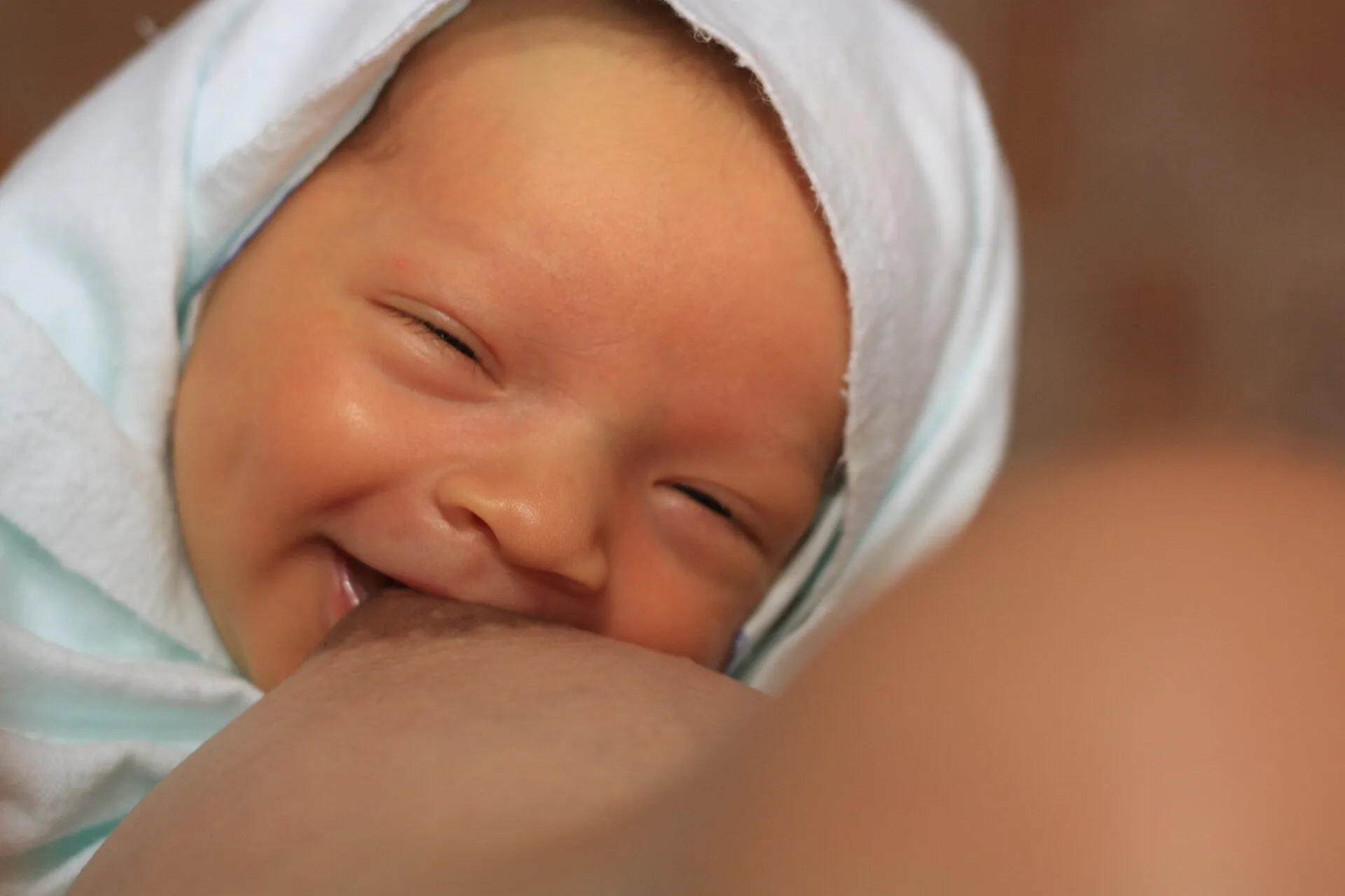 bebê sorrindo amamentando no peito, deitado no colo da mãe